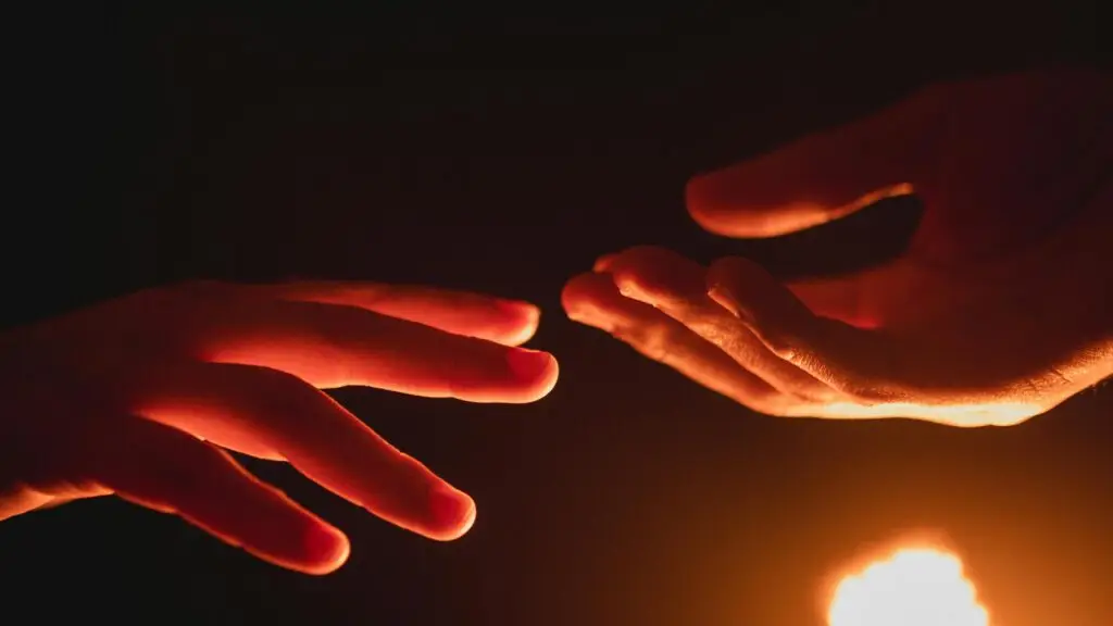 A close-up of two hands reaching towards each other in warm, glowing light.